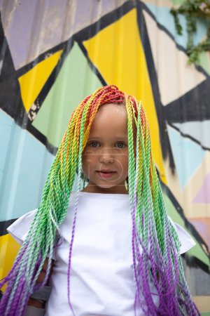 portrait of a little beautiful girl with multi-colored pigtails on the background of a colorful wall.