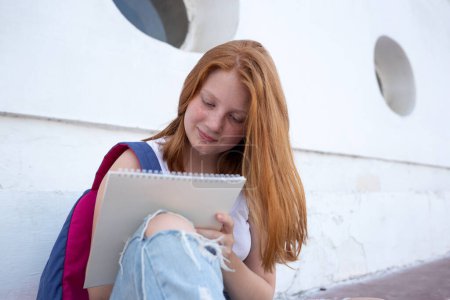 Téléchargez les photos : Adolescente dessine dans le carnet de croquis tout en étant assis sur les marches. - en image libre de droit