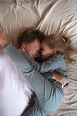 little cute girl hugging her dad while lying in bed.