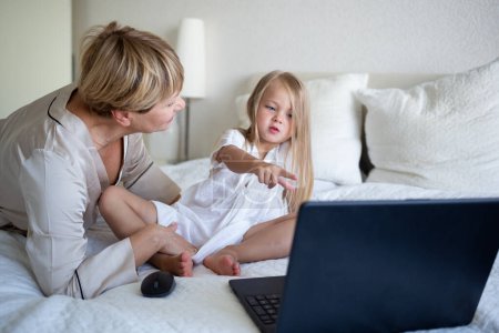 little girl with her grandmother sitting on the bed in front of a laptop.