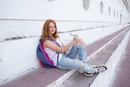 teenage girl draws in the sketchbook while sitting on the steps.