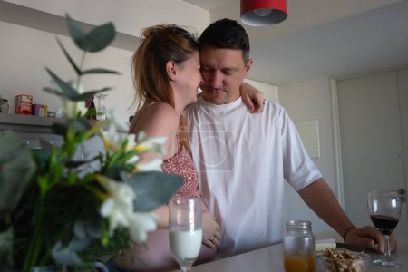 A happy couple in the kitchen, laughing and embracing, as they eagerly anticipate the arrival of their baby.