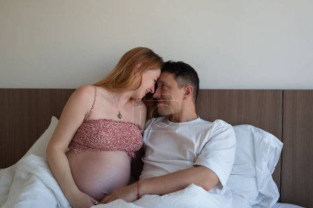 Ein liebendes Paar im Bett, das einen intimen Moment miteinander teilt, lächelnd auf die Ankunft ihres Babys wartet.