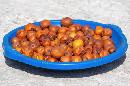 Red jujube fruits are being dried in a blue plastic bowl in the sun. Ziziphus mauritiana also known as Indian plum, Chinese date, and Chinese apple. It is locally called Kul or Boroi in Bangladesh.