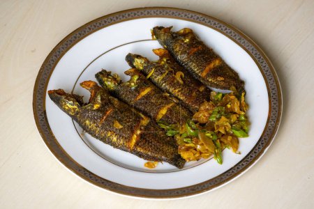 Foto de Delicioso pescado koi frito adornado con cebollas picadas y chiles verdes en un plato. El nombre científico de este pez es Anabas testudineus, comúnmente conocido como la perca trepadora.. - Imagen libre de derechos