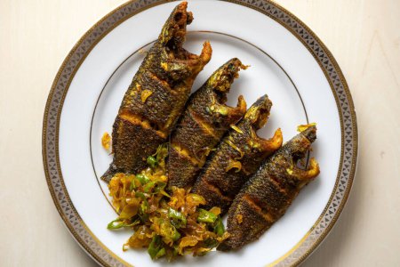 Köstlich gebratener Koi-Fisch, garniert mit gehackten Zwiebeln und grünen Chilischoten auf einem Teller. Der wissenschaftliche Name dieses Fisches ist Anabas testudineus, allgemein bekannt als der kletternde Barsch. Ansicht von oben.
