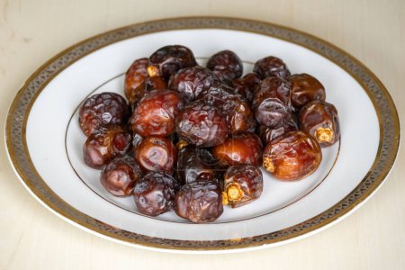 Delicious dried date palm fruits or kurma on a white plate on a wooden background. Locally in Bangladesh, it is called Khejur. Dates are high in fiber and antioxidants.
