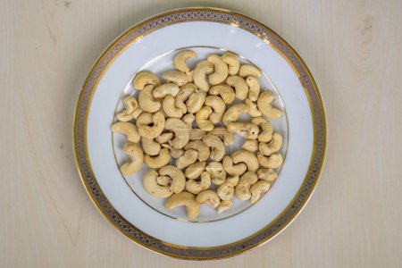 Cashew Nut (Anacardium occidentale) on a white plate. In the Bengali language, it is called Kaju Badam. Cashew nuts are high in fiber, heart-healthy fats, and plant protein. Top view.