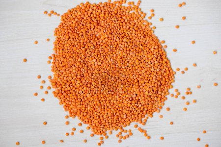 Scattered raw red lentils on a wooden table. Red lentils are also known as masoor dal, orange lentils, and pink lentils.
