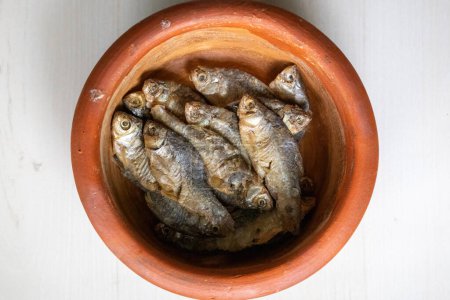 Puti poisson séché au soleil dans un pot en terre sur un fond texturé en bois. Localement au Bangladesh, il s'appelle Chepa Shutki et est également connu comme barbe de piscine, barbe argentée, barbe de marais à ailettes, barbe stigmatisée