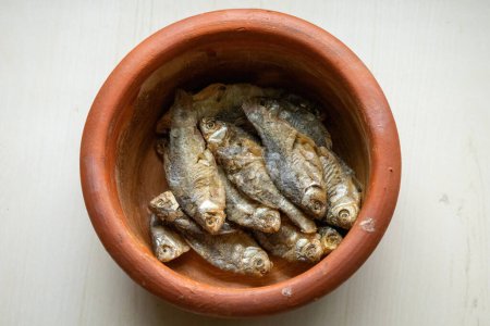 Sonnengetrockneter Puti-Fisch in einem irdenen Topf auf einem hölzernen strukturierten Hintergrund. Lokal in Bangladesch wird sie Chepa Shutki genannt und auch als Poolbarbe, Silberbarbe, Fleckflossensumpfbarbe, Stigma-Barbe bekannt