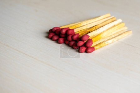 A pile of match sticks isolated on a wooden background. It is a short, slender piece of flammable wood used in making matches. It is useful for starting a fire, lighting a candle, burning paper, etc.