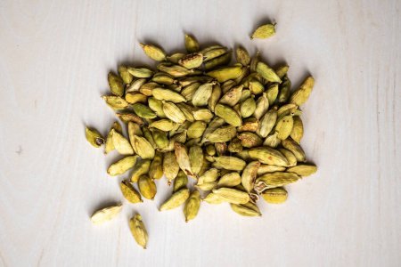 A pile of cardamom pods isolated on a wooden background. locally in Bangladesh, it is called Elachi and Its scientific name is Elettaria cardamomum. Top view.