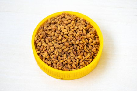 Fenugreek seeds on a yellow container on a white wooden background. Locally in Bangladesh, it is known as Methi Dana.