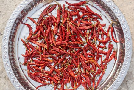 A pile of red chilies in a dish for making chili flakes or chili powder. Red peppers are being dried in the sun. Top view.