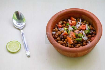 Gekochte Kichererbsen oder Chana in einem irdenen Topf auf Holzgrund. Gehackte Tomaten, Zwiebeln und grüne Chilischoten gemischt mit bengalischem Gramm. Chola Boot ist ein gesundes Nahrungsmittel, das reich an Proteinen ist. Gewichtsverlust Mahlzeit