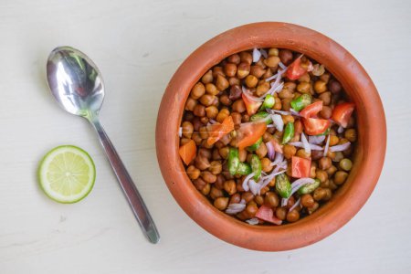 Garbanzos hervidos en una olla de barro sobre fondo de madera. Tomates picados, cebolla y chiles verdes mezclados con el gramo de Bengala. Comida saludable para perder peso. Localmente en Bangladesh, se llama Chola Boot.