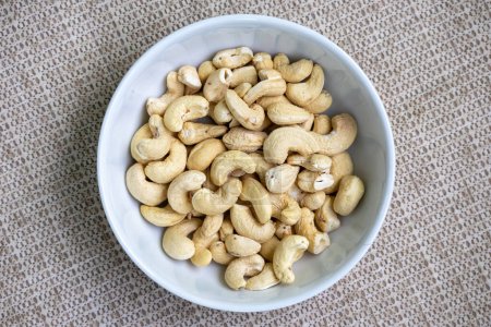 Tasty cashew nuts in a white bowl on a beautiful textured background. Its scientific name is Anacardium occidentale and In the Bengali language, it is called Kaju Badam. Top view.