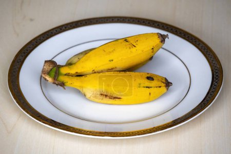 Gelbe reife Bananen auf einem weißen Teller zum Frühstück. Die morgendliche Bananendiät kann bei der Gewichtsabnahme helfen, da Bananen reich an Ballaststoffen sind, die Ihnen helfen, satt zu bleiben.