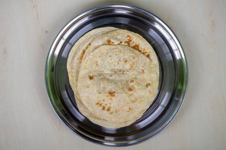 Pan plano de trigo integral o roti en un plato de acero sobre fondo de madera. Sabrosa comida bengalí (Bangladesh) que a menudo se come con verduras o carne. En Bangladesh, se llama Ruti. Vista superior
