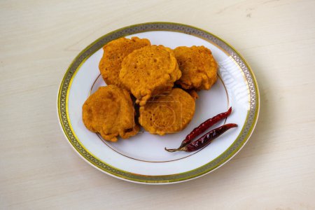 Hausgemachte leckere Aloo Chop mit gerösteten trockenen Chilischoten auf einem weißen Teller auf Holzgrund. Alu Chop ist ein beliebter Snack aus Bangladesch und der bengalischen Region Indien.