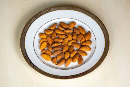 Raw almonds on white plate on wooden background. Almond nuts are healthy food. 