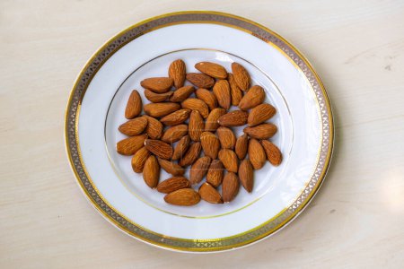 Raw almond nuts on white plate on wooden background. Almonds are a healthful food. 