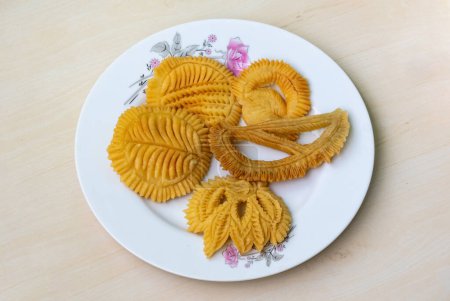 Crispy Nakshi Pitha on a white plate on wooden background. It is a traditional Bengali (Bangladesh) food, also known as Pakkon Pitha. This type of pitha is made from rice flour.