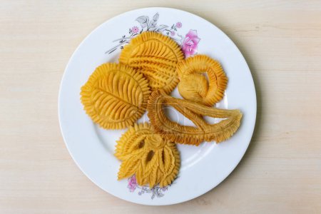 Nakshi Pitha or Pakkon Pitha on a white plate on wooden background. It is a traditional Bengali (Bangladesh) food, also known as Pakkon Pitha. This type of pitha is made from rice flour. Top view.