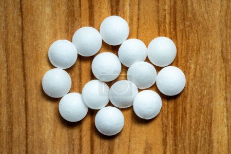 Bolas de naftaleno blanco aisladas sobre fondo de madera. También se conoce como escamas de polilla, naftalina, antimita y hexaleno. Vista superior