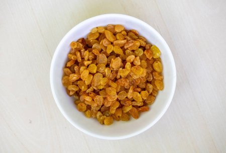 Delicious raisins in a white bowl on wooden background. Raisins are dried grapes. Its scientific name is Vitis vinifera. In the Bengali language, it is called Kismis or Kishmish. Top view