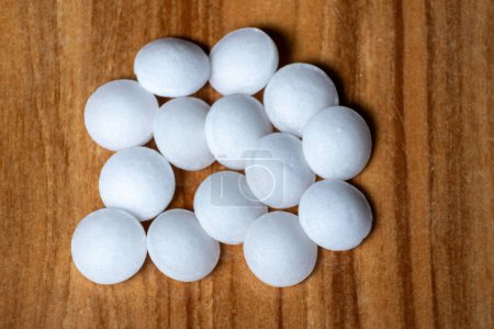 Many Naphthalene mothballs isolated on wooden background. It is also known as moth flakes, naphthalin, antimite, and hexalene.