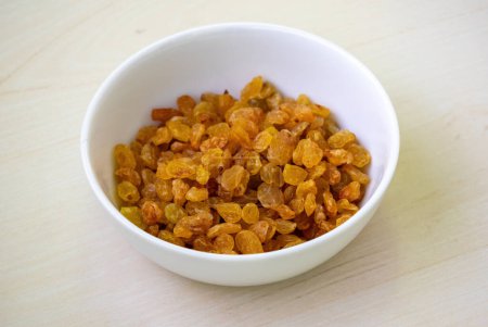 Delicious raisins (Vitis vinifera) in a white bowl on wooden background.