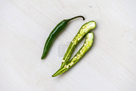 One whole green chilli and one chilli cut in half on wooden surface. Top view