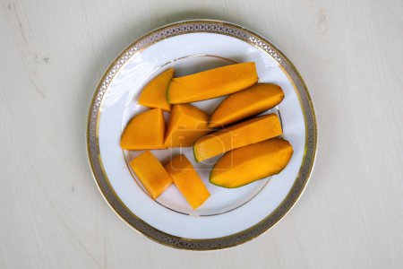 Ripe mango slices on a white plate on wooden background. Top view.