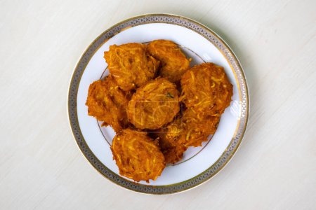 Homemade delicious Pakora on a white plate on a wooden background. Top view. Homemade delicious Pakora on a white plate on a wooden background. Pakora is a popular snack food from Bangladesh and the Bengal region of India.