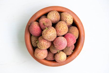 A clay pot filled with delicious ripe lychees. The lychees have a reddish-brown textured skin. Lychees are a healthy tropical fruit.