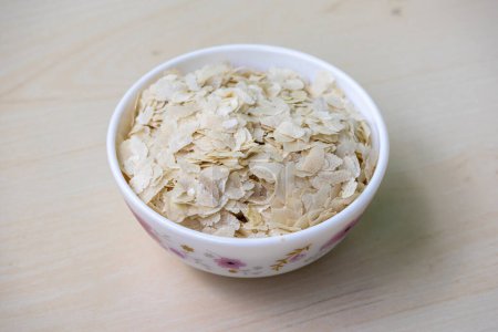Arroz aplanado o Chira en un tazón blanco sobre una superficie de madera. También se conoce como pohe, aval, pauwa, sira, chivda, o avalakki.