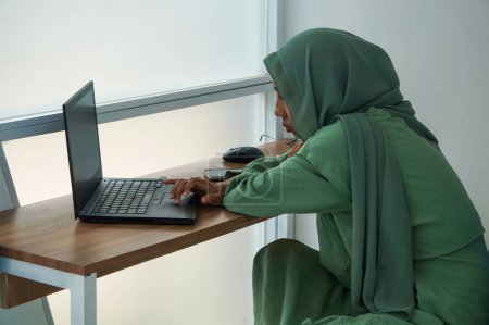 Foto de Una mujer musulmana que trabaja en casa usando un portátil - Imagen libre de derechos