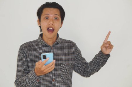 Junger asiatischer Mann hält Smartphone in der Hand und zeigt mit dem Finger zur Seite