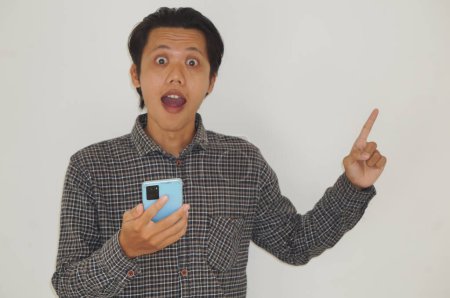 Young asian man holding smartphone and pointing with hand finger to the side