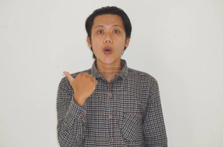 Photo for Young asian man wearing black shirt surprised pointing with hand finger to the side - Royalty Free Image