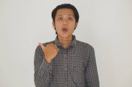 Photo for Young asian man wearing black shirt surprised pointing with hand finger to the side - Royalty Free Image