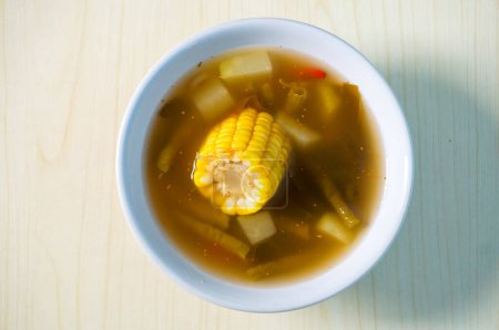 Indonesian traditional food named "sayur asem" with ingredient slices of chayote, corn, tamarind, long beans, chili pepper, bilimbi served on bowl isolated on wooden background