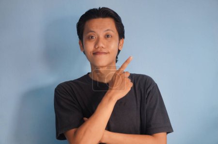 Photo for Young asian man wearing a black t-shirt smiling pointing with hand finger to the side. - Royalty Free Image