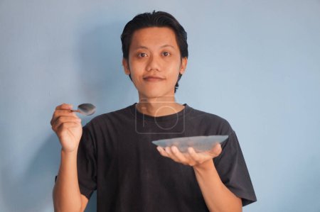 Joven asiático vistiendo camiseta negra sosteniendo plato de cena y cuchara