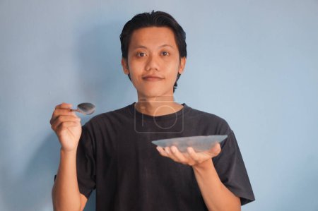 Young Asian man wearing black t-shirt holding dinner plate and spoon