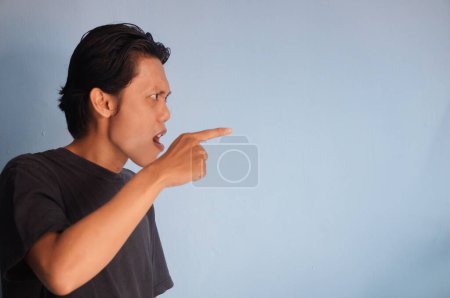 junger asiatischer Mann in schwarzem Hemd wütend, indem er auf die Seite zeigt