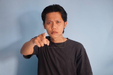 young asian man wearing black t-shirt angry by pointing at camera