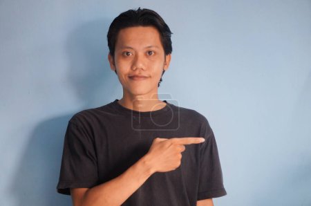 Photo for Young asian man wearing black t-shirt smiling pointing with hand finger to the side - Royalty Free Image